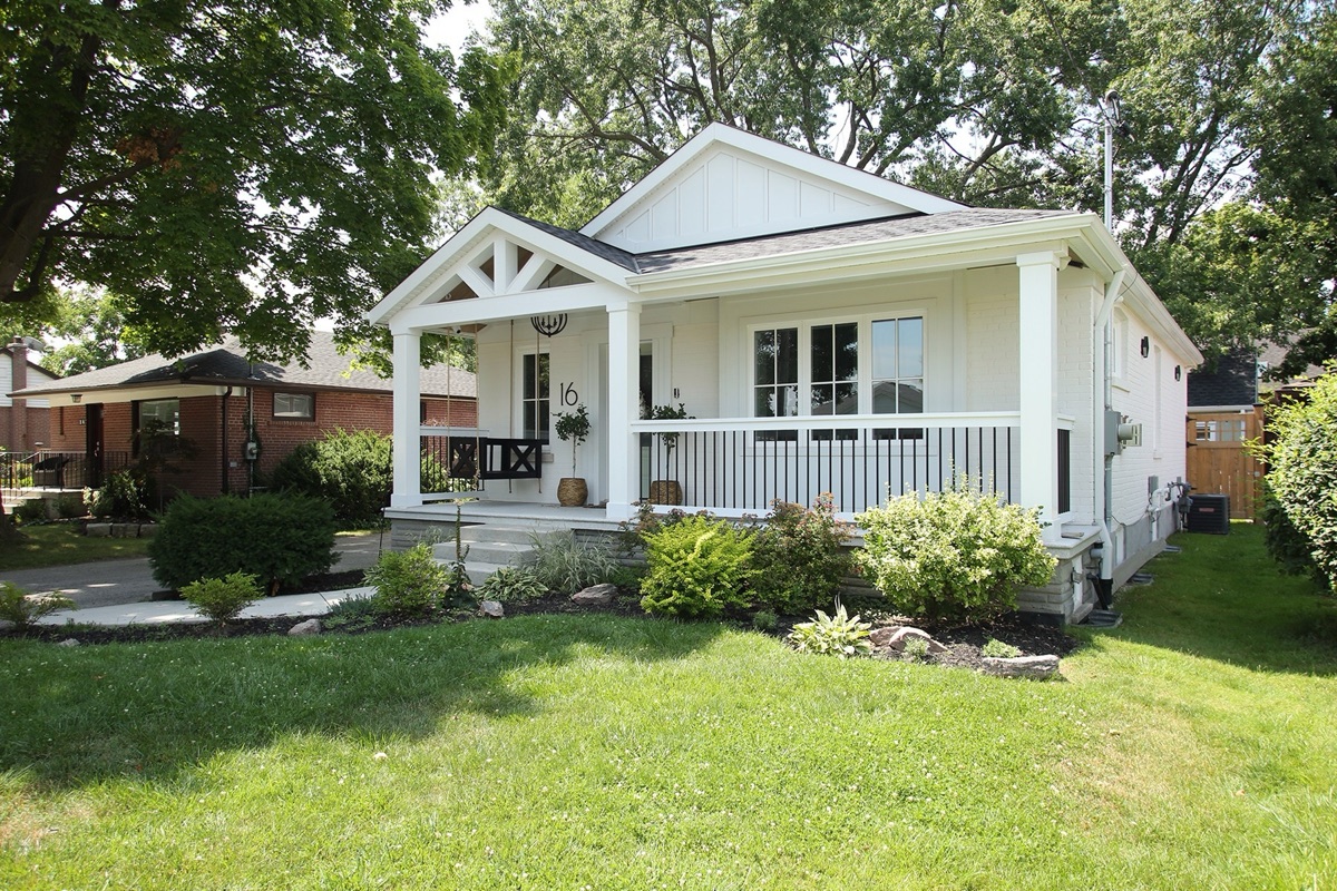 Front exterior of a white bungalow in Etobicoke with a covered porch, gabled entry, and landscaped beds.