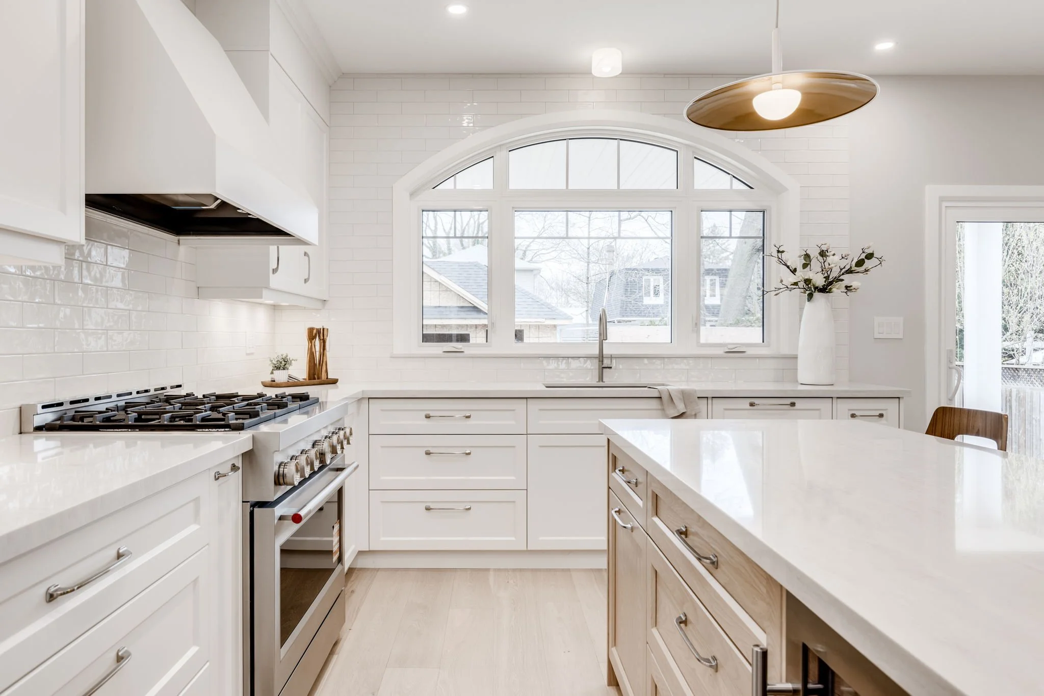 White kitchen with an arched window over the sink, gas range, and a wood-panelled island
