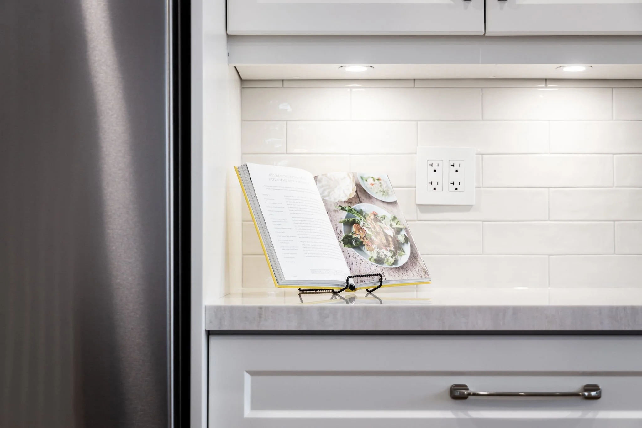 Cookbook stand and reading glasses on a kitchen counter under cabinet lighting