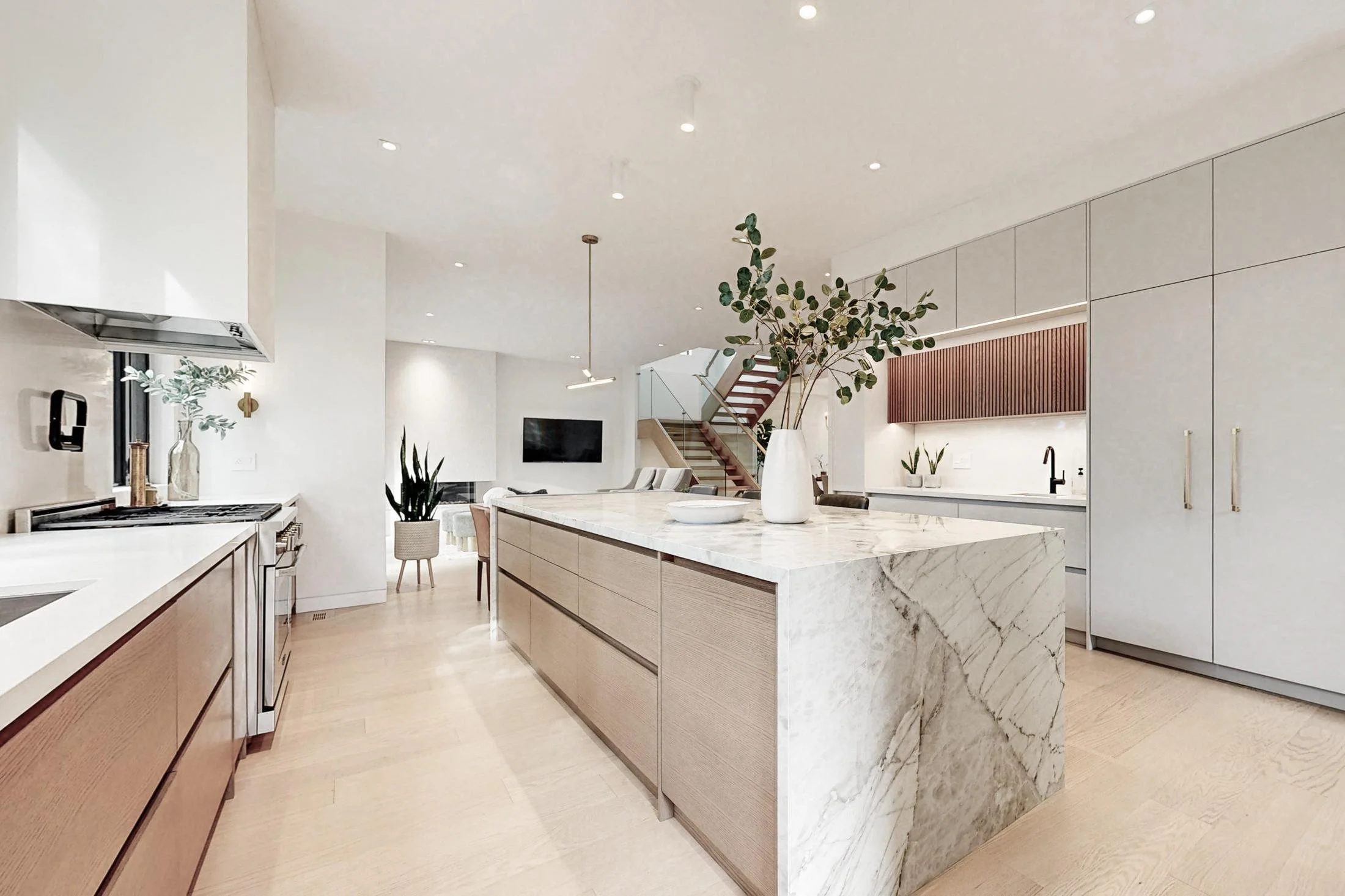 Open-concept kitchen with a waterfall marble island, wood lower cabinets, and a staircase beyond the dining area