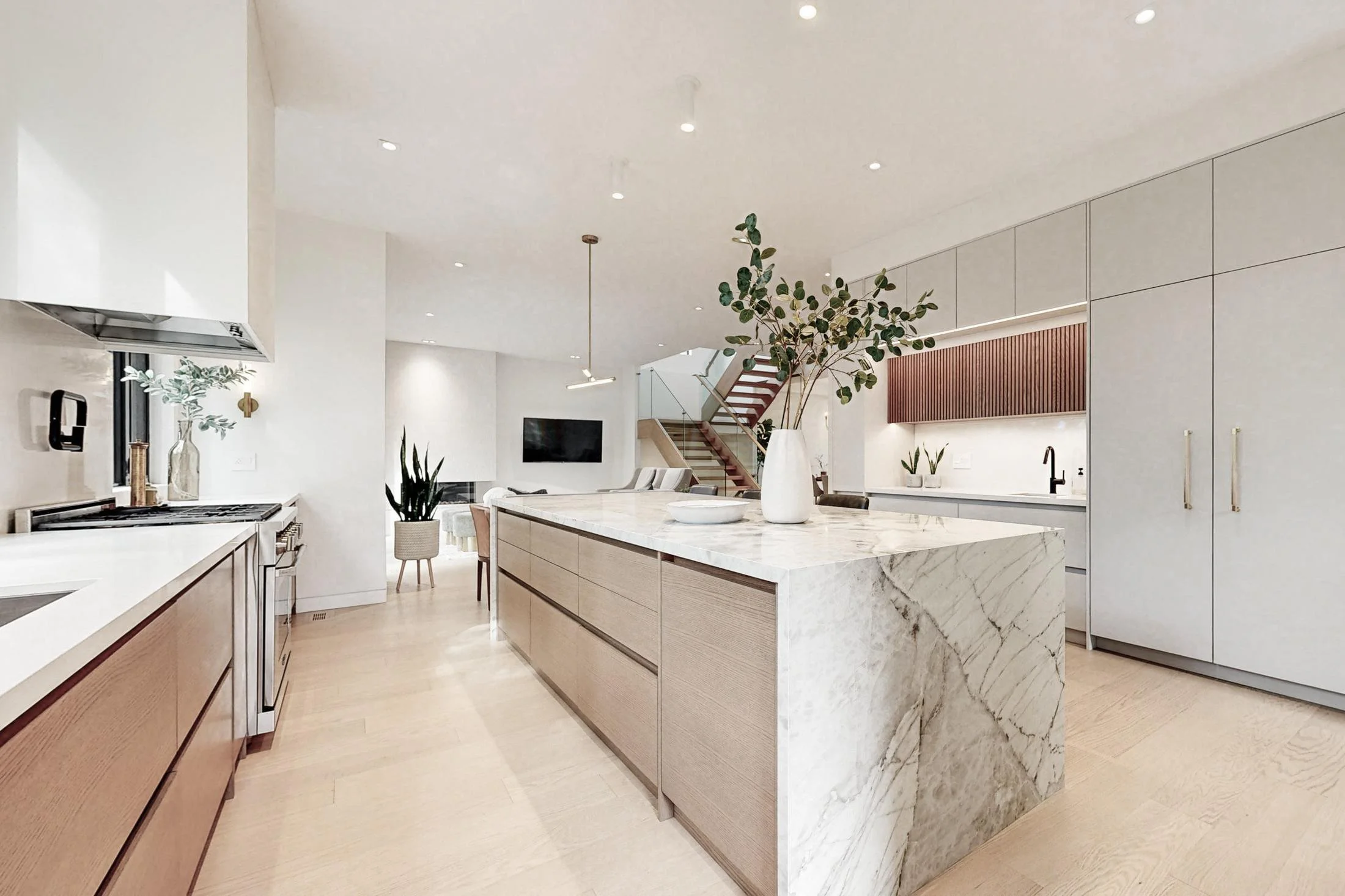 Open-concept kitchen with a waterfall marble island, wood lower cabinets, and a staircase beyond the dining area