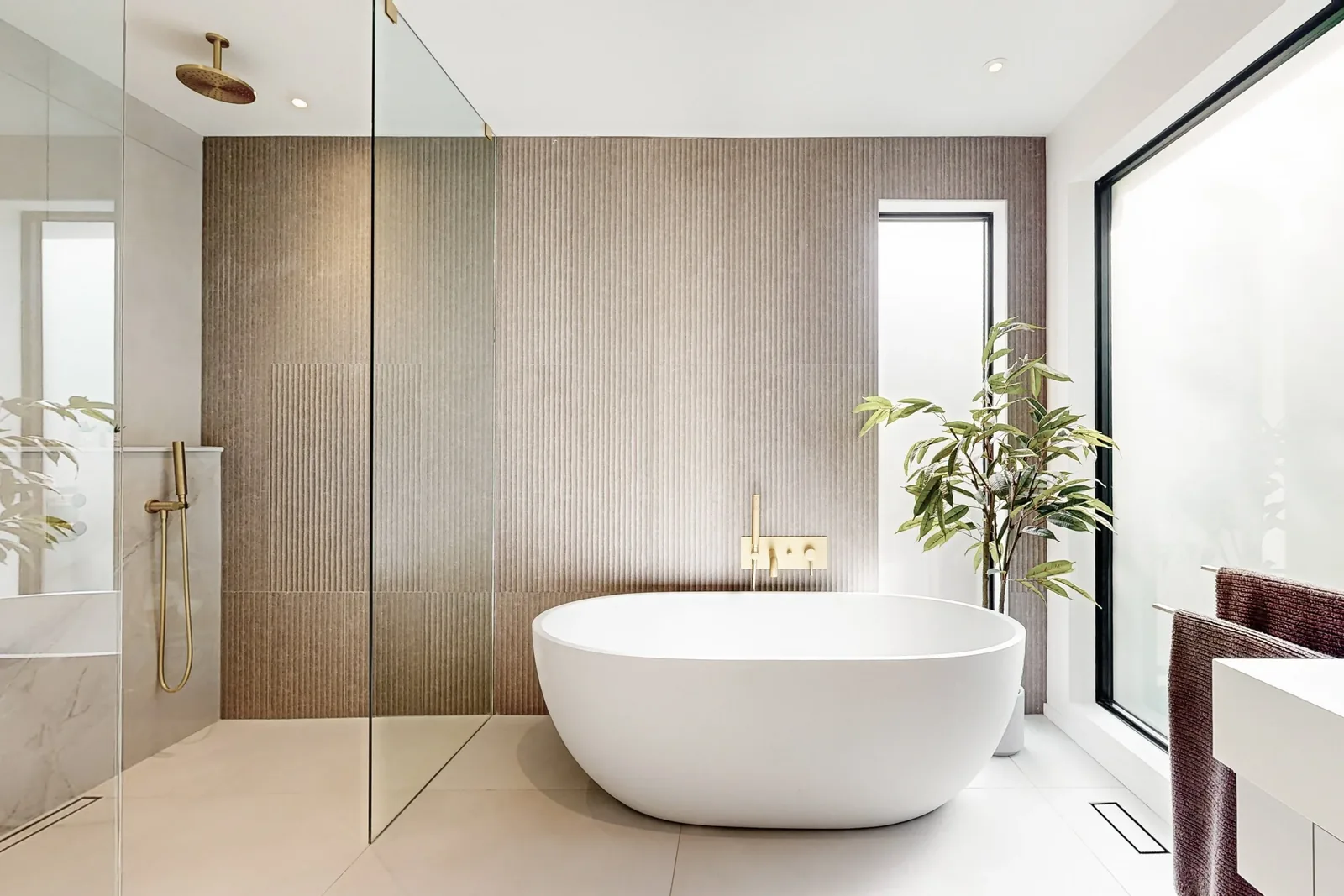 Modern bathroom with a freestanding white bathtub, textured beige wall, large windows, indoor plant, and glass shower area.