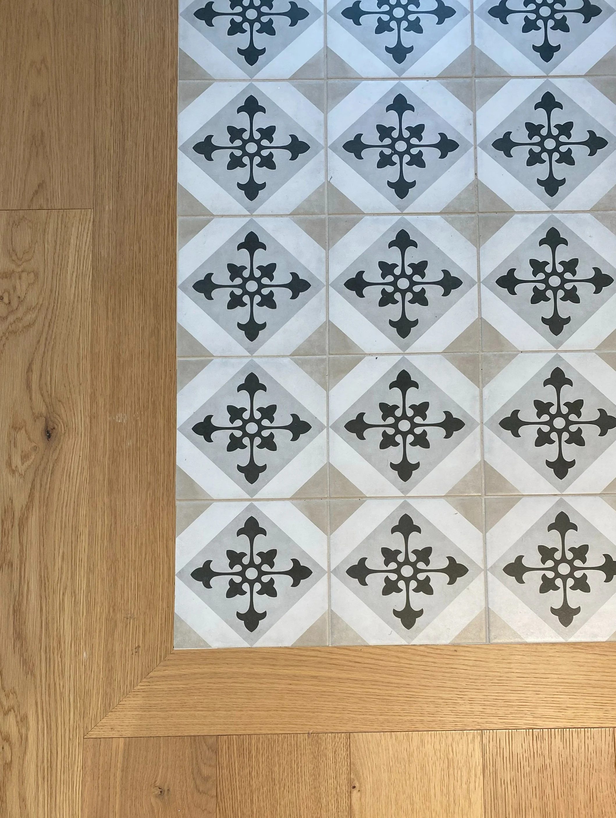 A section of floor with decorative black and white patterned tiles bordered by a wooden floor.