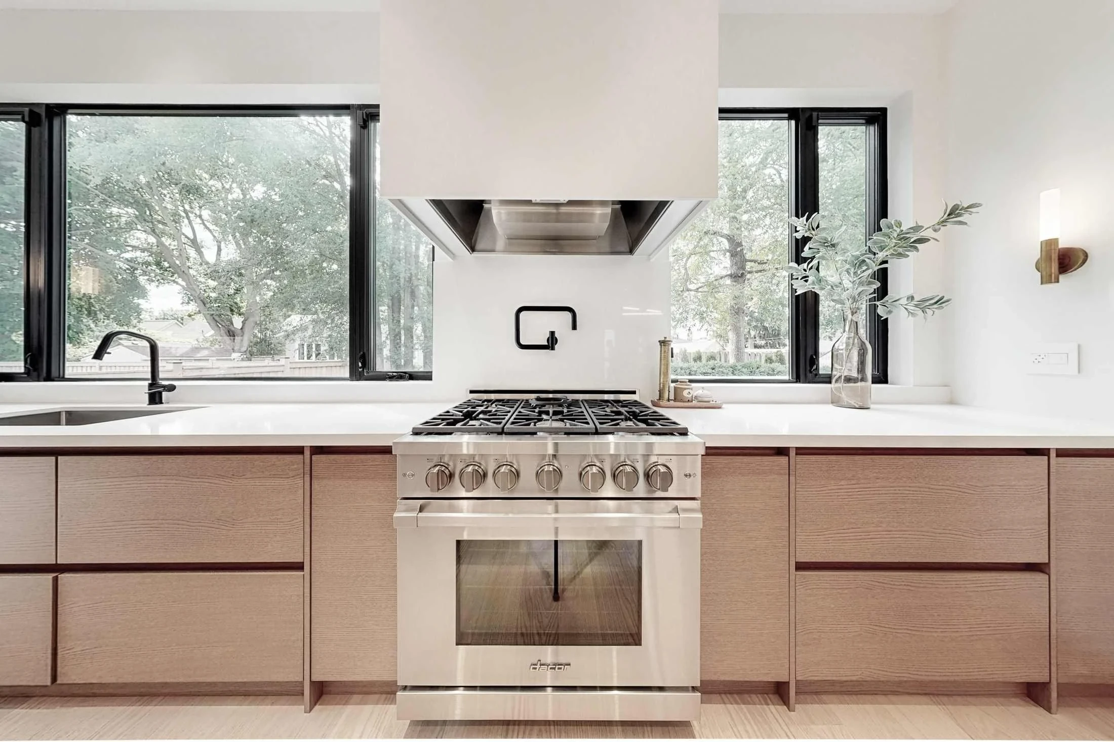 Gas cooktop in the foreground looks across an open-concept living room with a linear fireplace, wall TV, and cognac lounge chairs.