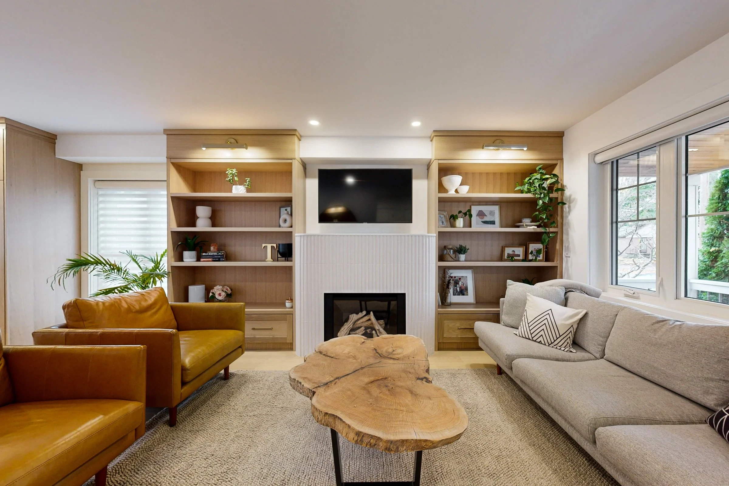 Bright renovated living room with oak built-ins, a fireplace wall, and neutral seating by large windows.