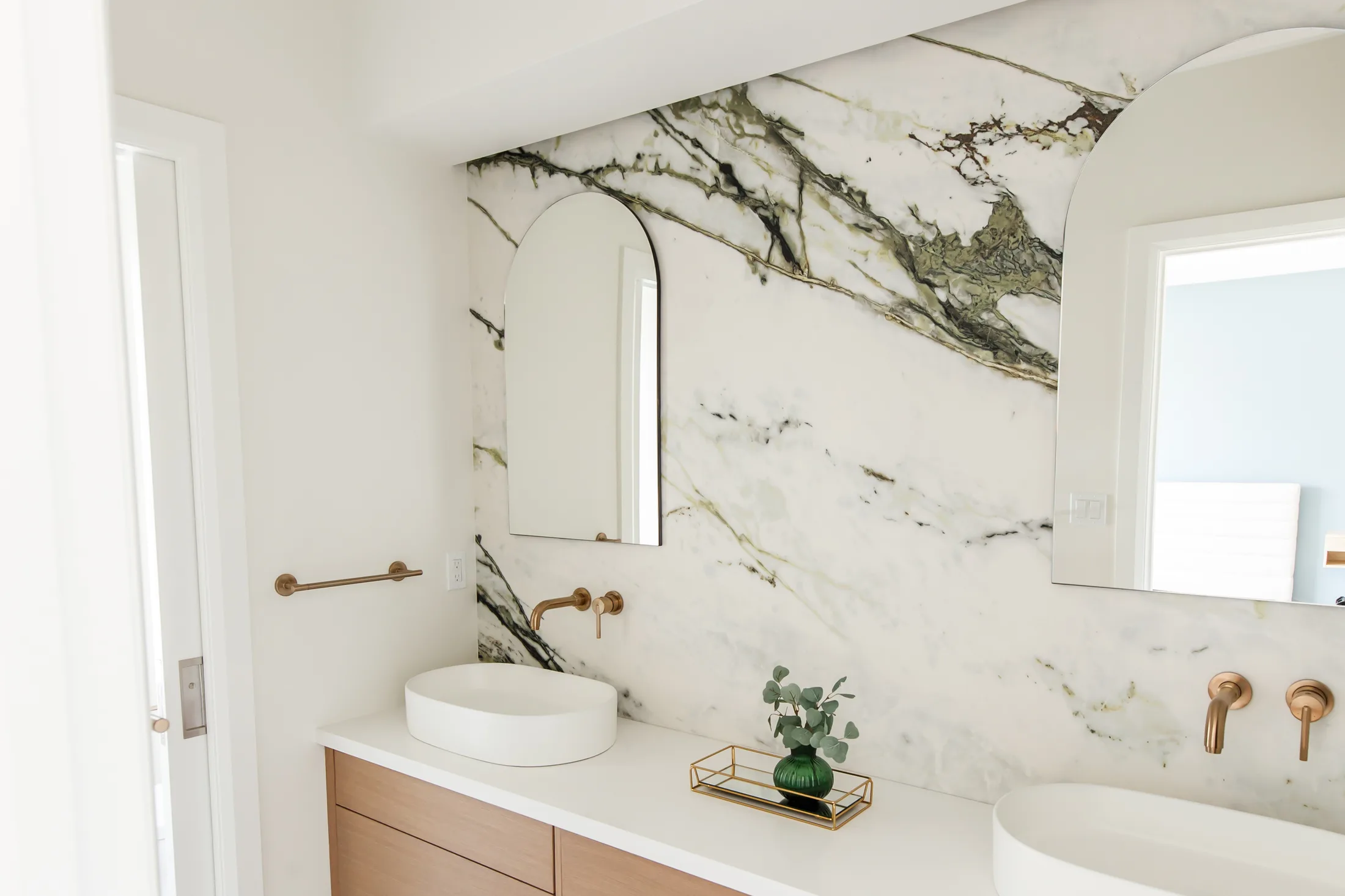 Modern bathroom with book-matched marble slab, floating oak vanity and twin vessel sinks.