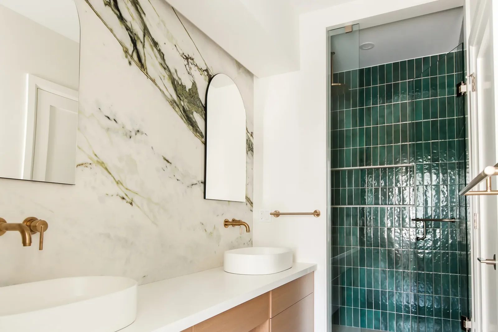 Primary bath with marble vanity wall and emerald tile shower behind clear glass.