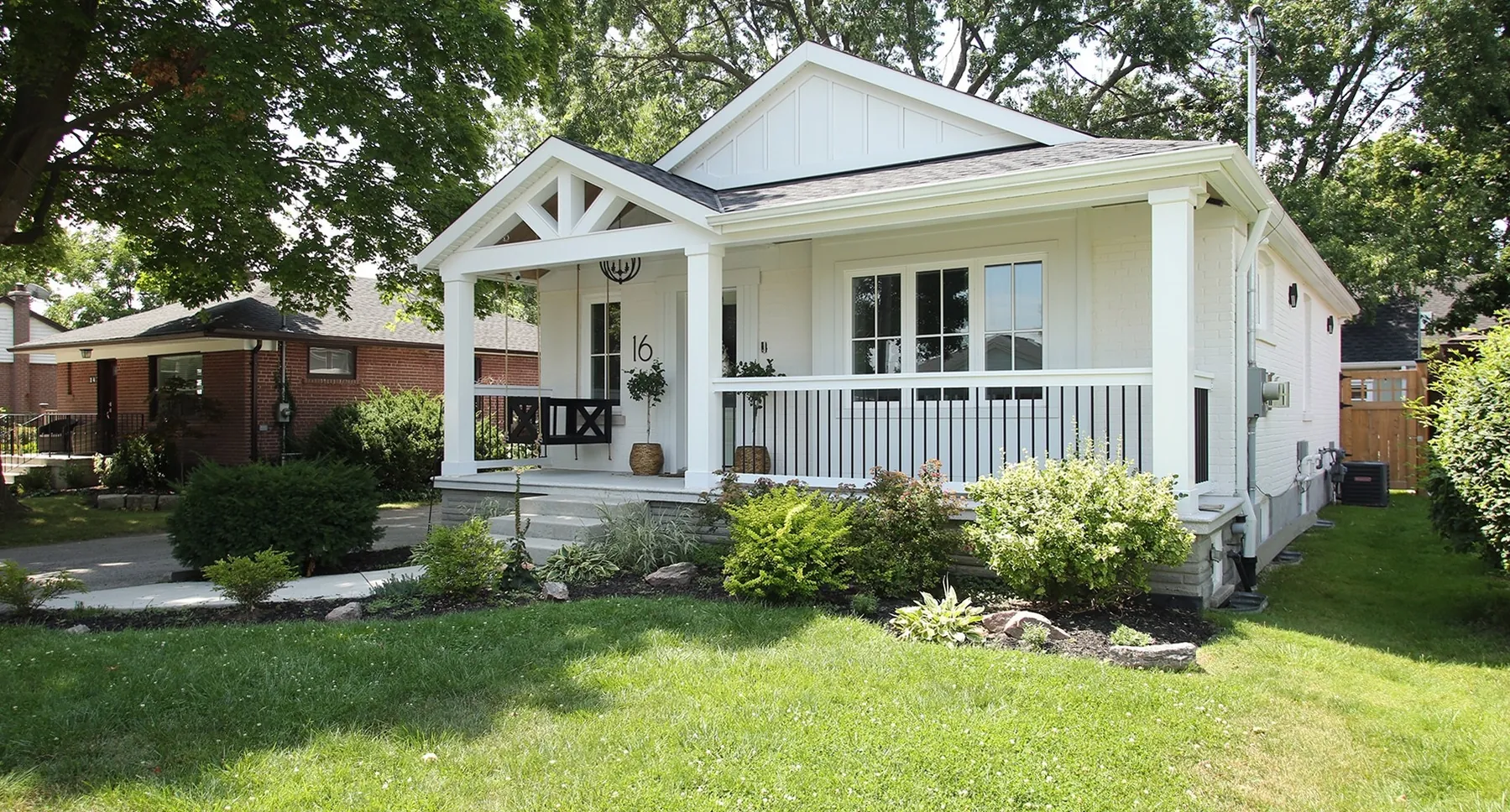 Completed white bungalow exterior with a covered gabled porch, black accents, and landscaped garden beds.