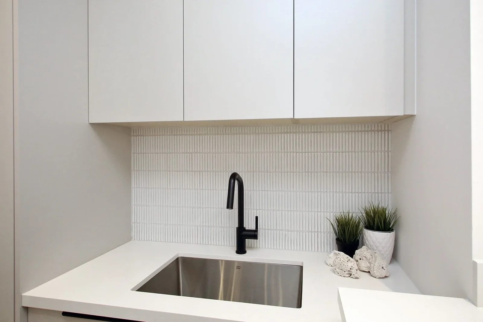Matte white laundry wet counter with a black faucet over a stainless sink against a vertical kit-kat tile backsplash.