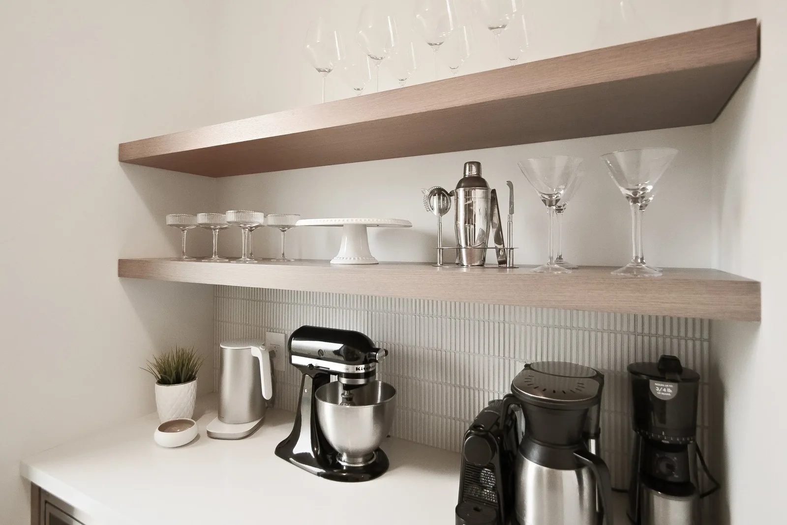 Butler pantry detail with floating oak shelves styled glassware and stacked white tile backsplash.