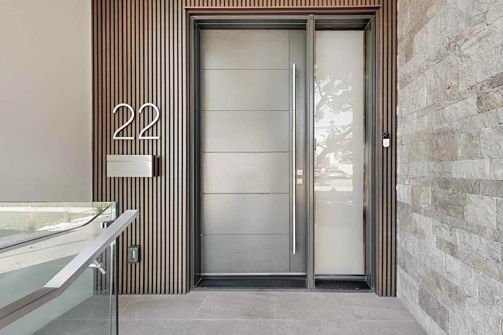 Front entry with a stainless steel pivot door framed by vertical wood slats and stone cladding, Casa Marbella project