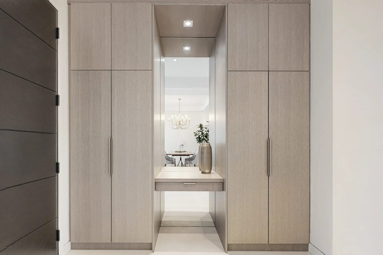 Symmetrical oak wardrobe wall with a mirrored centre niche reflecting the dining chandelier.