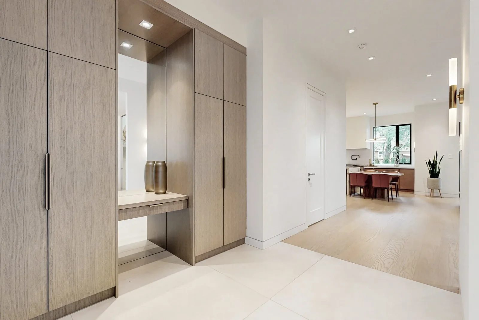 Wide foyer view along oak wardrobe wall with kitchen and dining visible at the far end of the home.