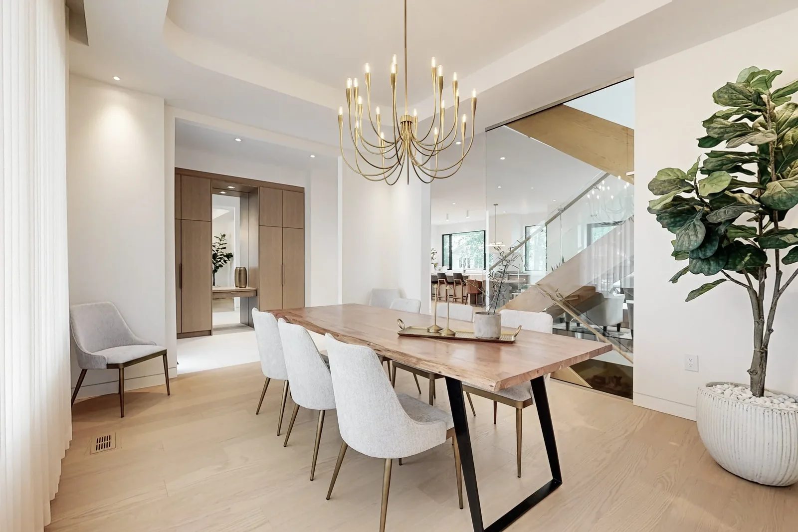 Dining room with a live edge wood table surrounded by grey upholstered chairs under a brass candelabra chandelier.