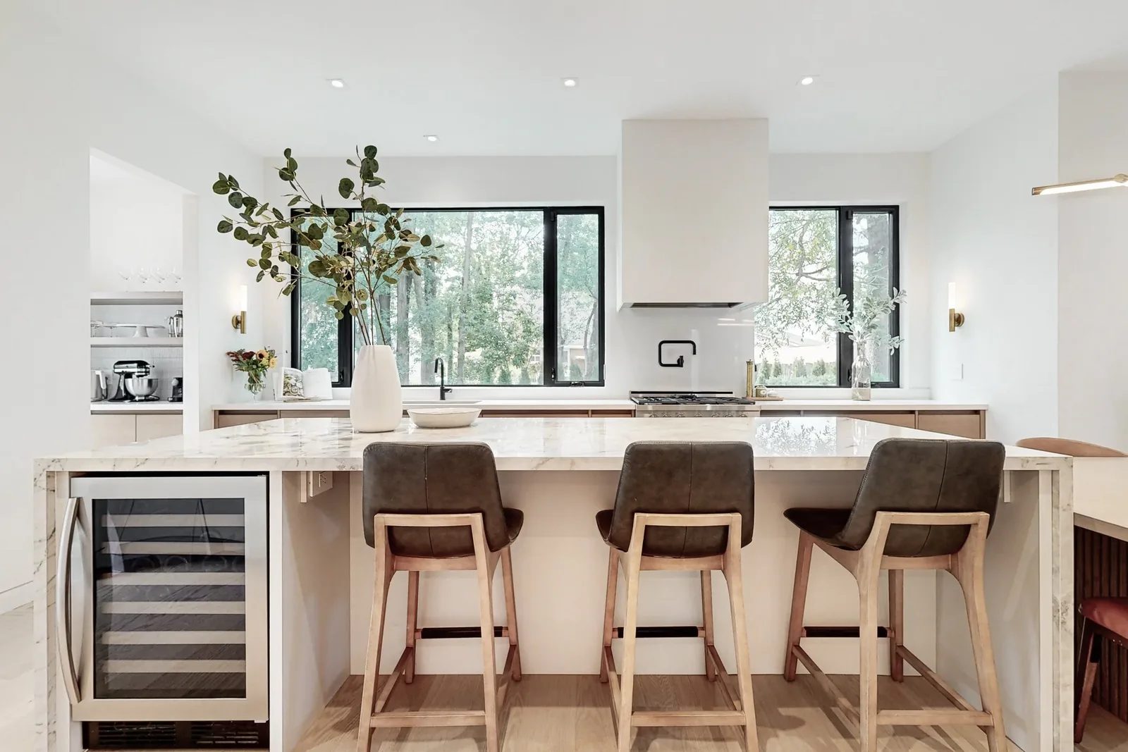 Luxury kitchen island in calacatta marble with waterfall edge leather barstools and black framed windows over the range.