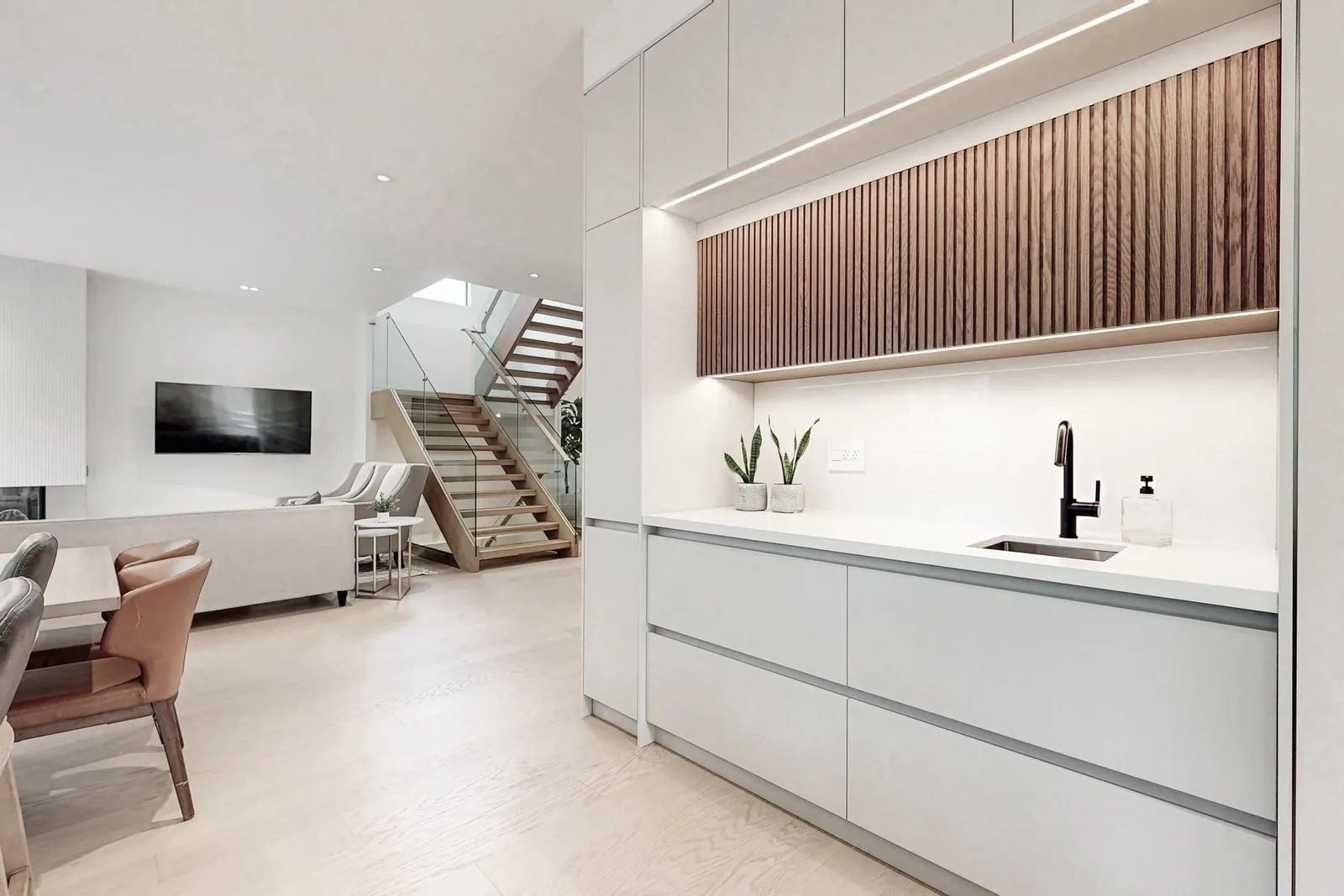 Open concept sightline from servery wall through living room to an open riser staircase under skylight.