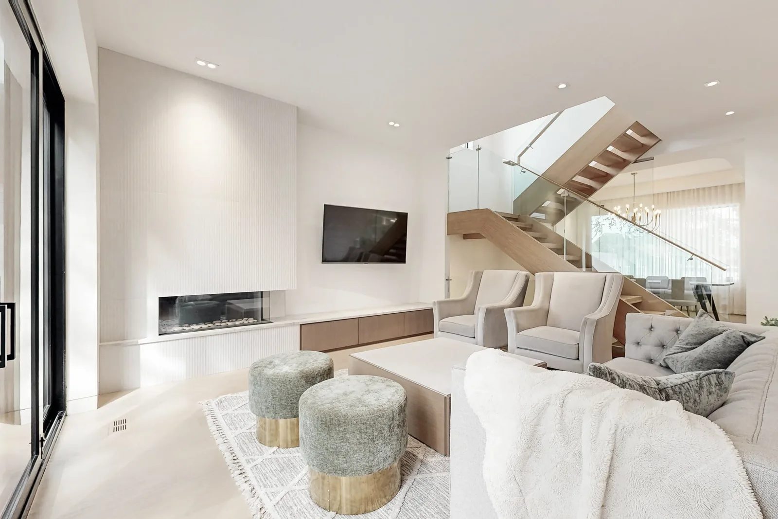 Living room with tufted sofa, velvet ottomans, and fluted tile fireplace beside a floating oak and glass staircase.