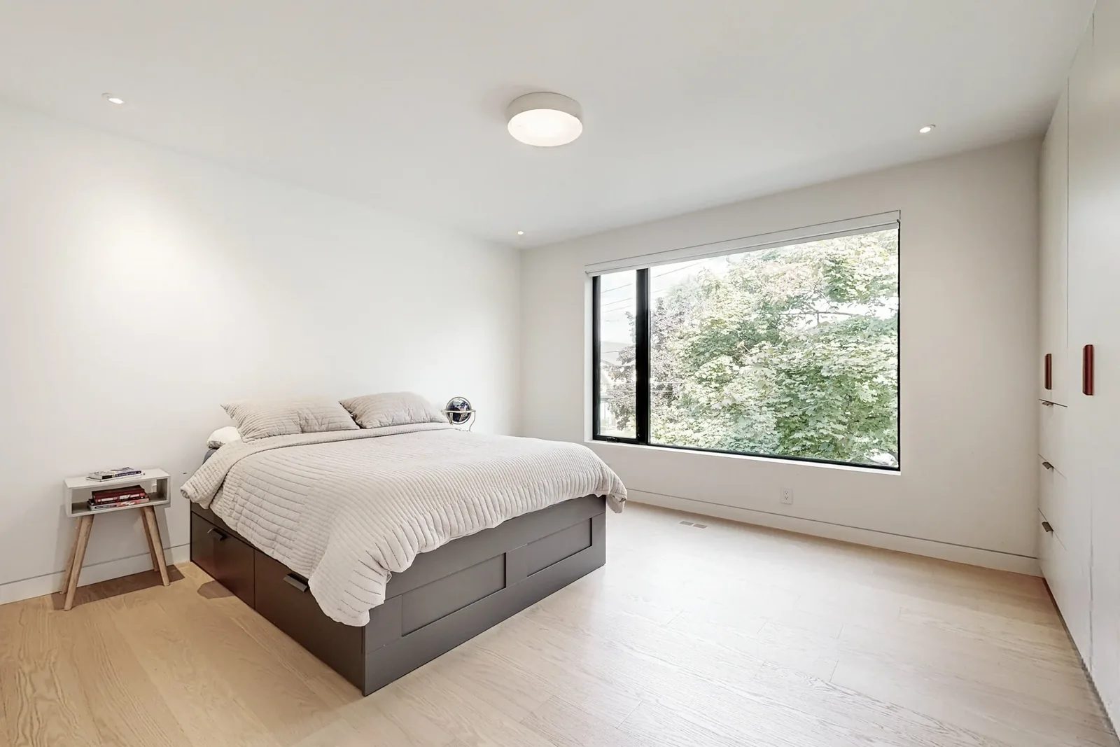 Bedroom with dark grey storage bed, built-in wardrobe, and a large black-framed picture window overlooking trees.