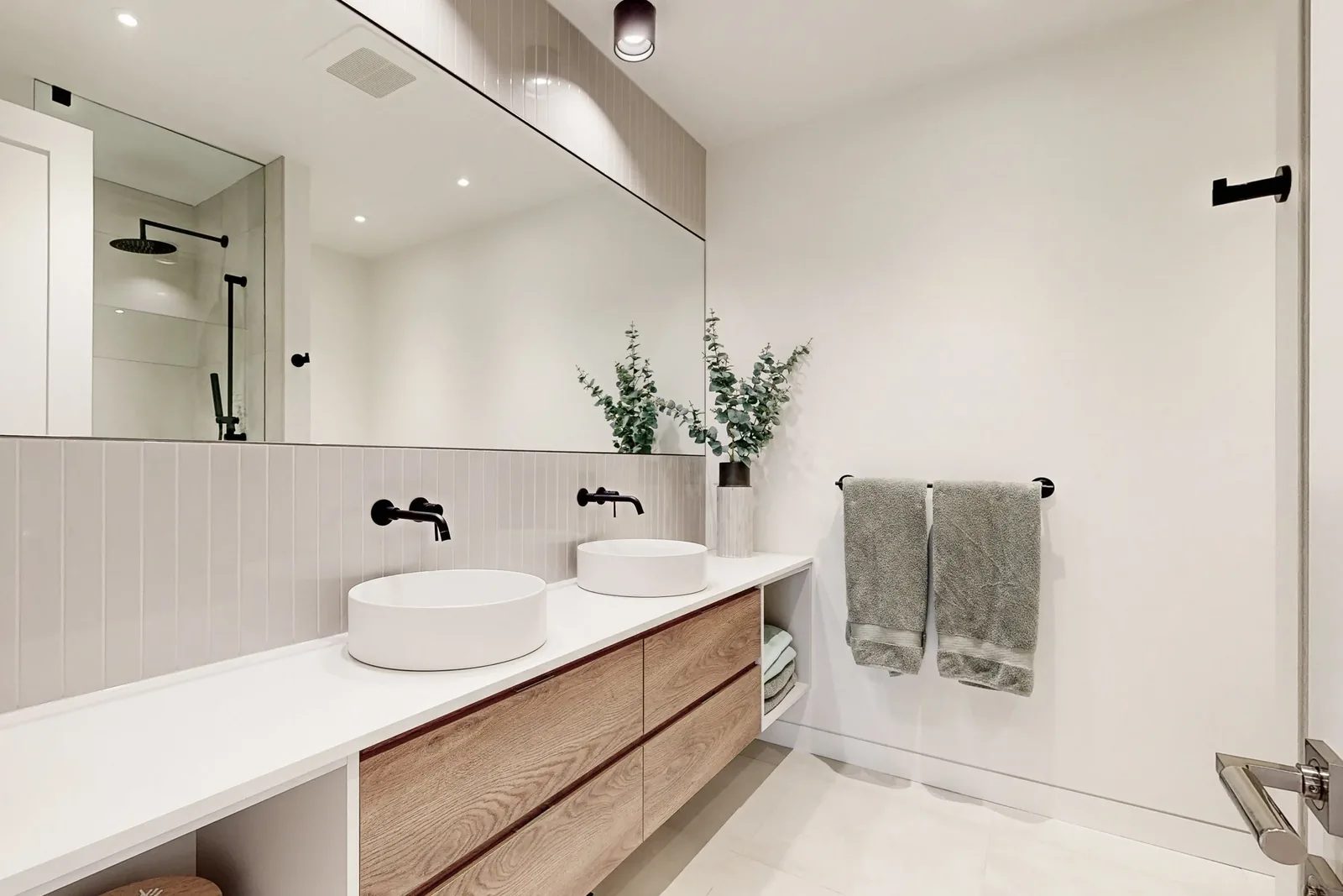 Family bathroom with wood-grain double vanity, twin vessel sinks, matte black faucets, and walk-in glass shower.