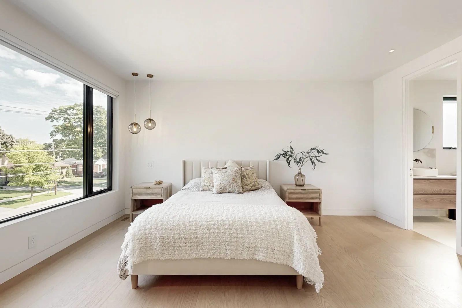 Principal bedroom with channel tufted bed framed by twin glass pendants and a large picture window.