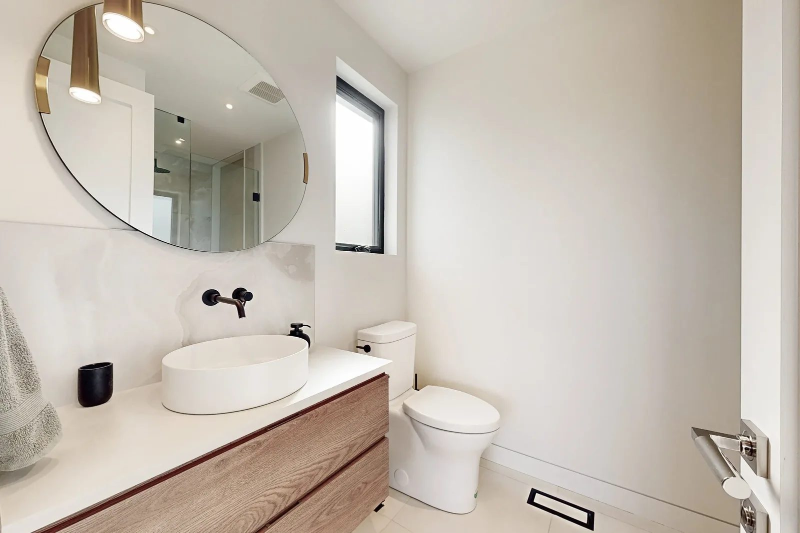 Powder room with floating oak vanity, onyx look stone slab and a round mirror flanked by brass pendants.