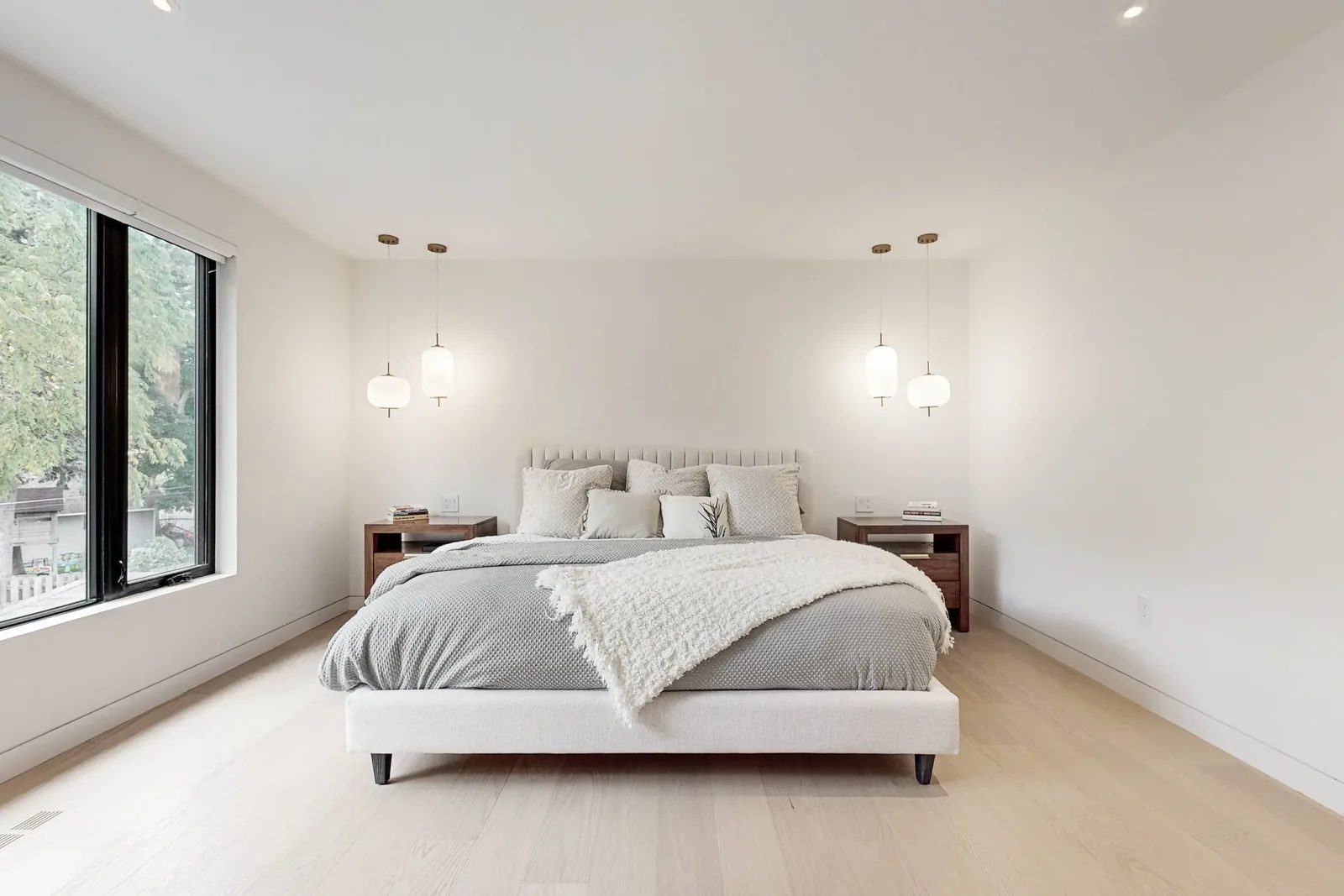 Principal bedroom with channel upholstered bed framed by matched walnut nightstands and pendant pairs.
