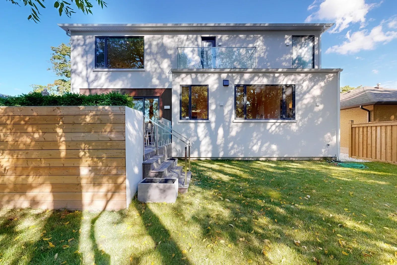 Full rear facade of the two-storey custom build with white stucco a cedar slat privacy screen and a concrete stair leading to the entry.
