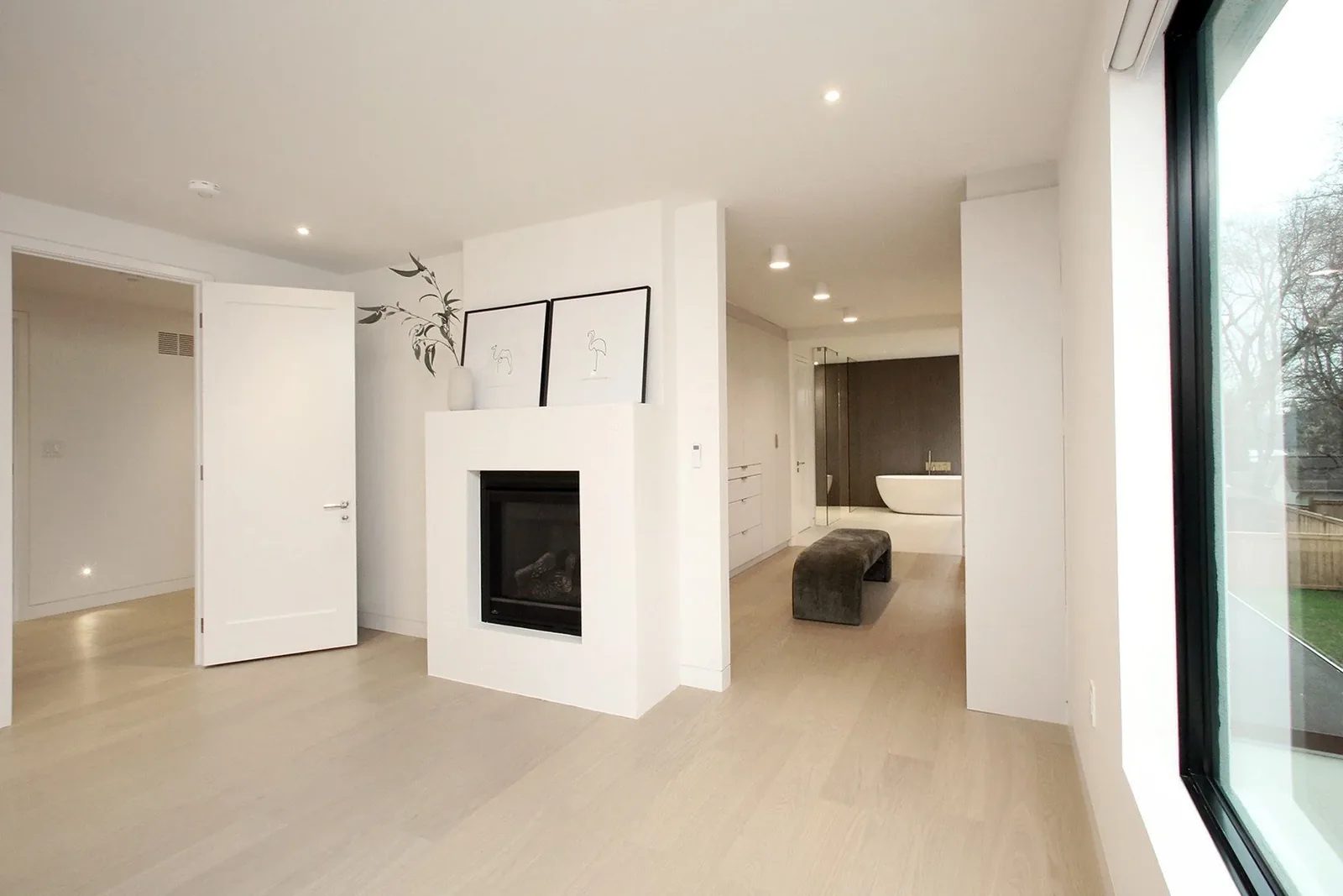 Primary suite looking across a fireplace partition through the walk in closet to the freestanding ensuite tub.