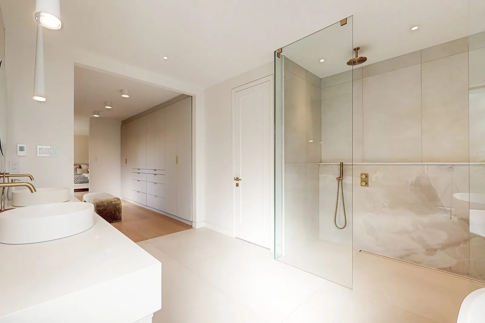 Wide view of a primary ensuite with a frameless glass walk-in shower onyx-look stone wall and open sightline through to the bedroom.