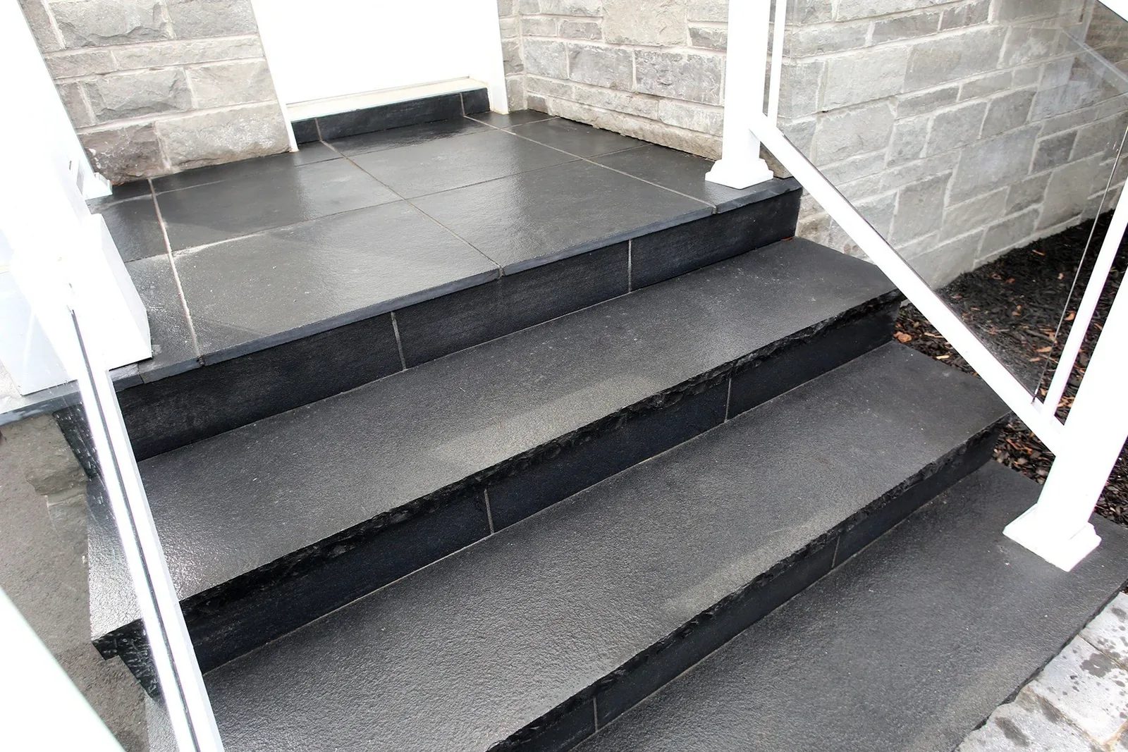 Charcoal stone front steps rise to a small entry landing, bordered by white railings and grey stone walls.
