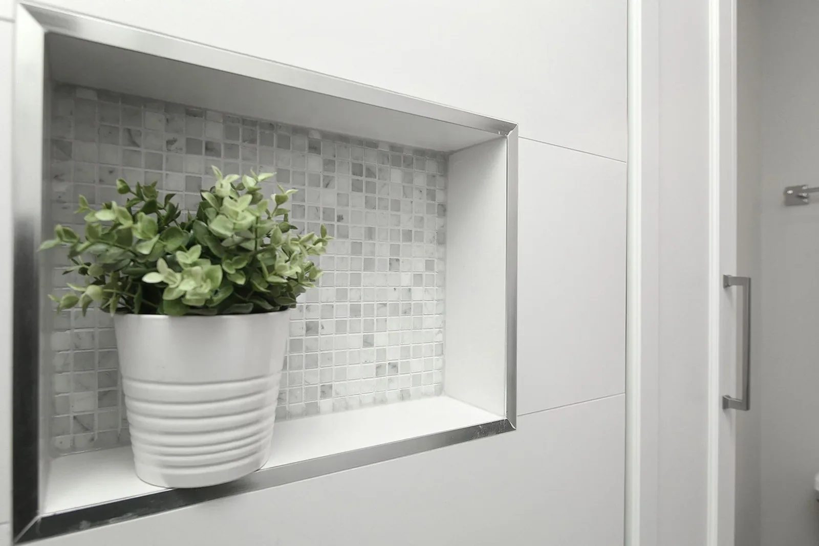 Bright shower niche with mosaic tile, white wall tile, and a small potted plant in a clean bathroom.
