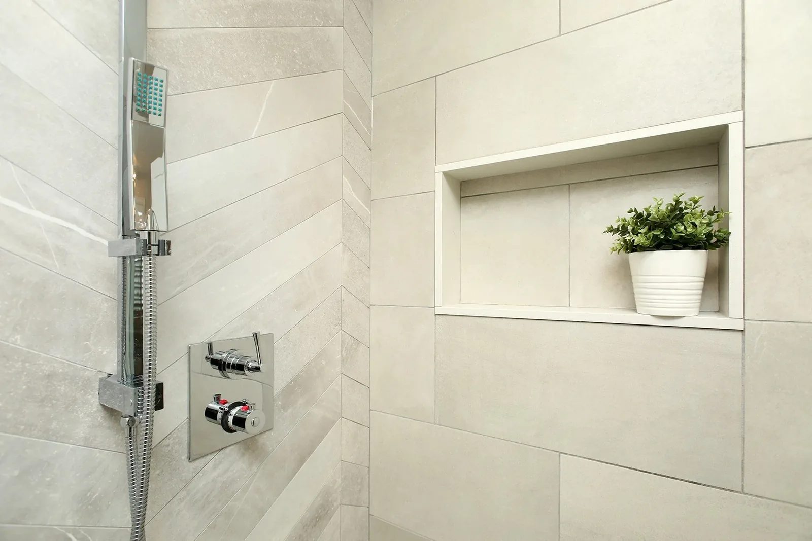Warm white shower with large-format tile, chrome fixtures, and a recessed niche with a small potted plant.