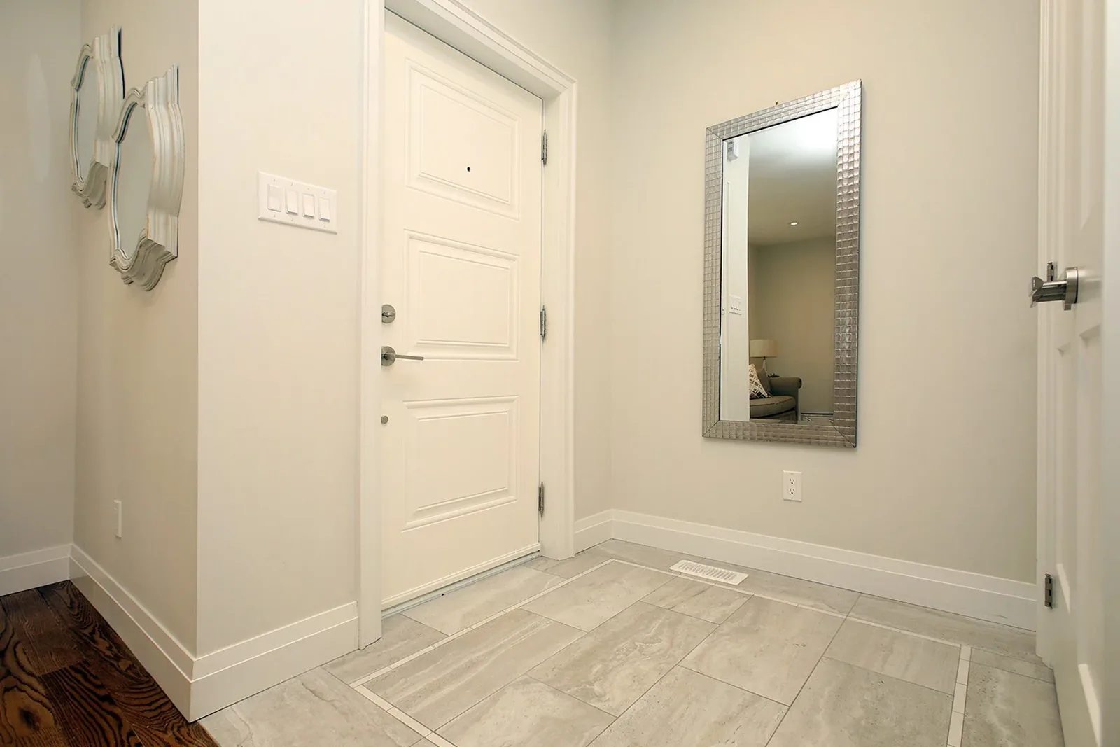 Bright entry with a large mirror, pale tile flooring, white trim, and dark hardwood beyond.
