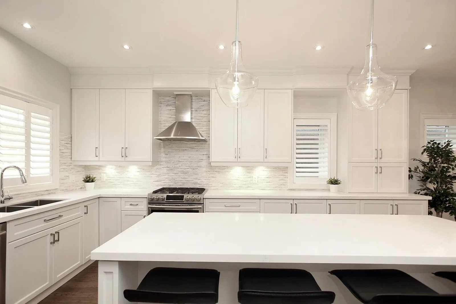 Bright white kitchen renovation with a large quartz island, shaker cabinets and glass pendants.