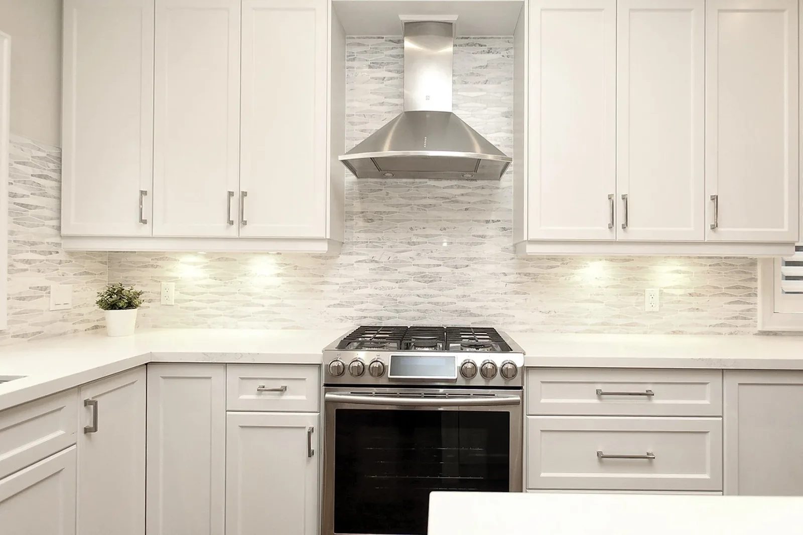 Warm white kitchen with shaker cabinets, quartz counters, mosaic tile backsplash and a centred steel range hood.