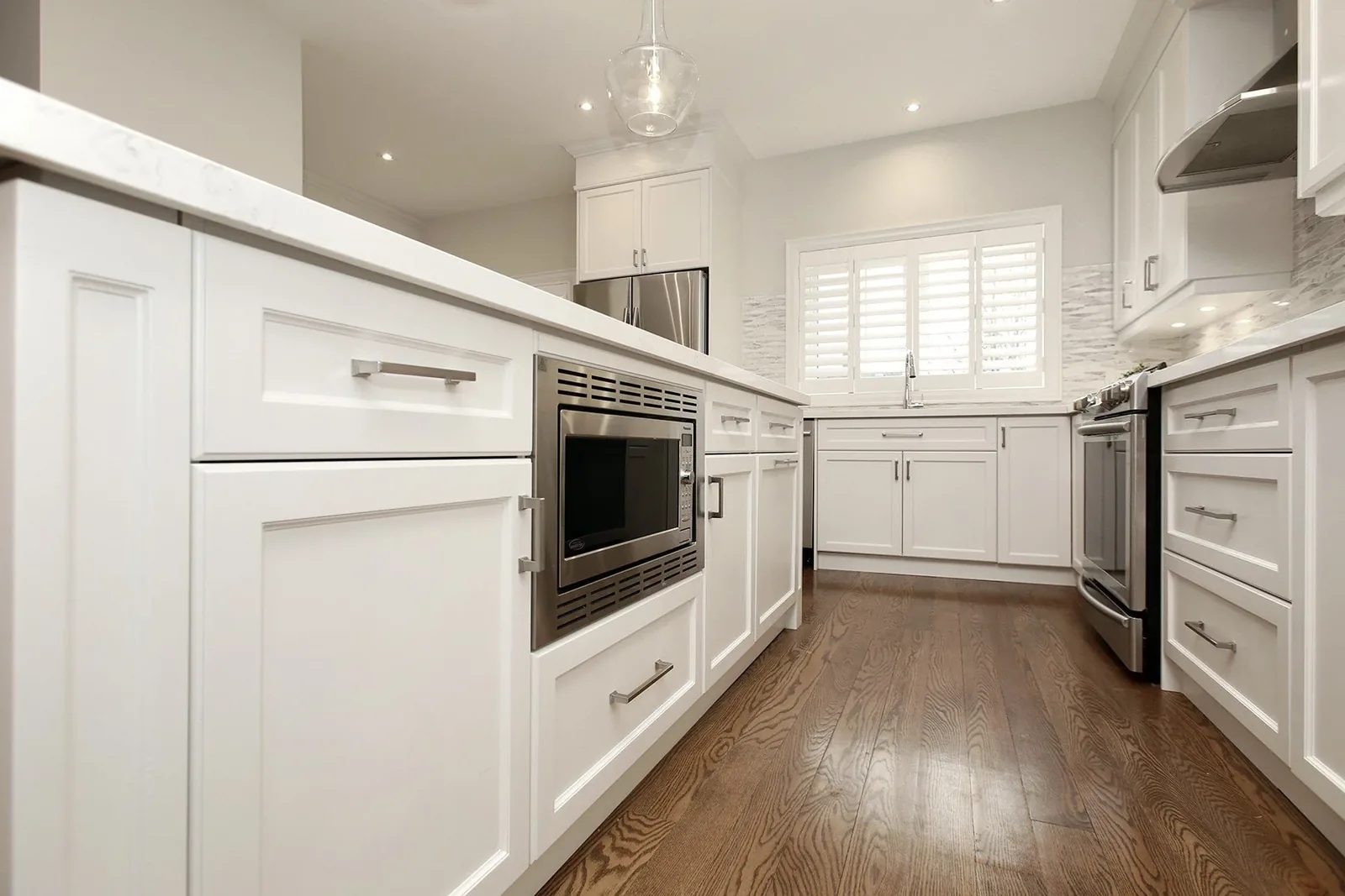 Bright renovated kitchen with white shaker cabinets, quartz counters, dark wood floors, and stainless appliances.