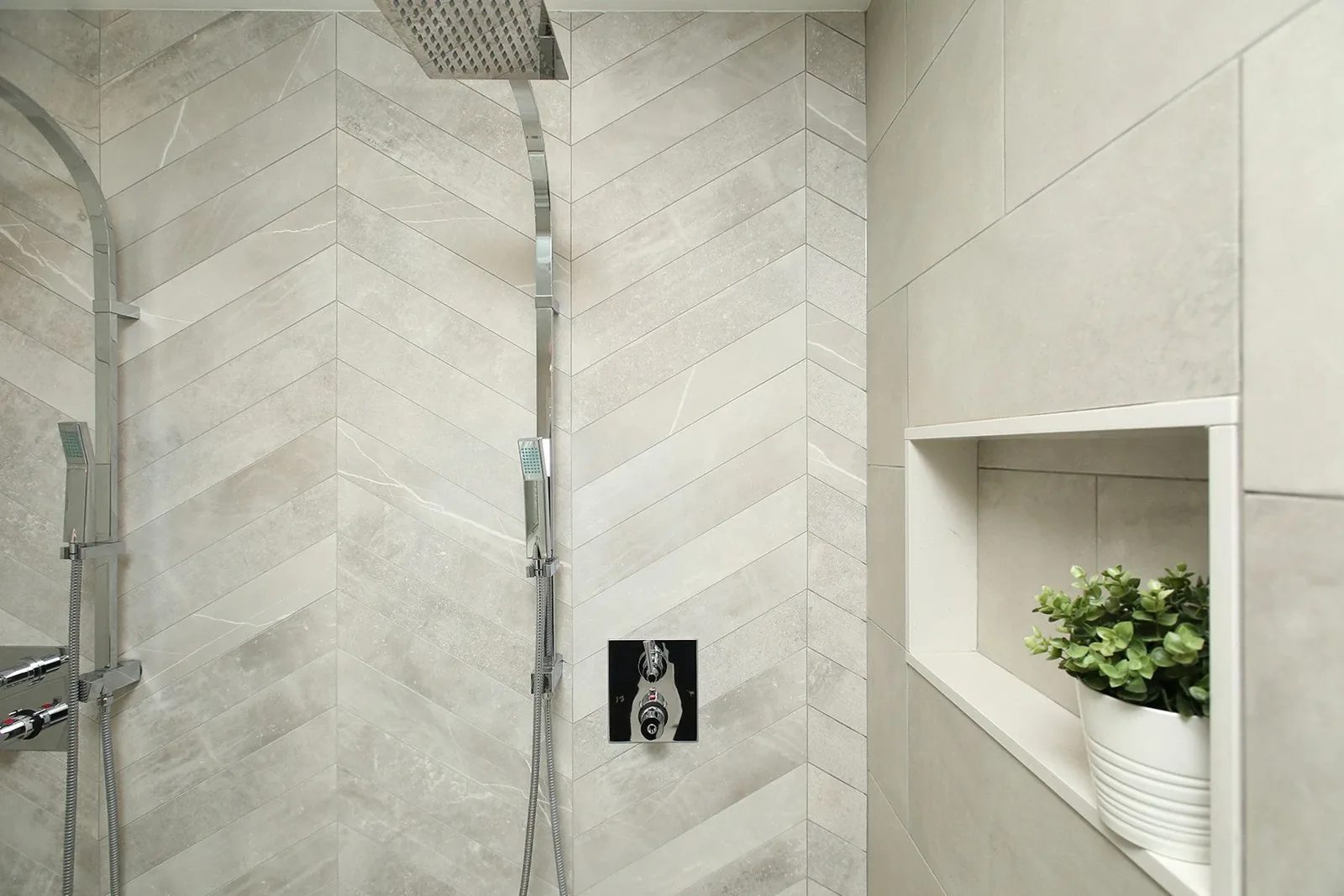 Bright shower renovation with light greige tile, chrome fixtures, and a recessed niche with greenery.