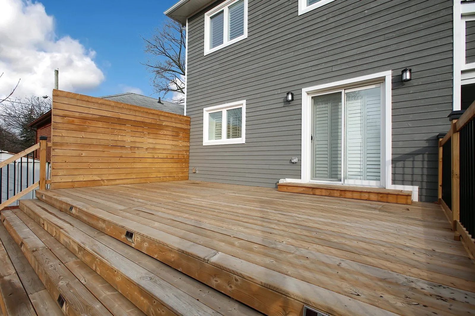 Large cedar deck with privacy screen and steps at the rear of a charcoal grey Toronto home.