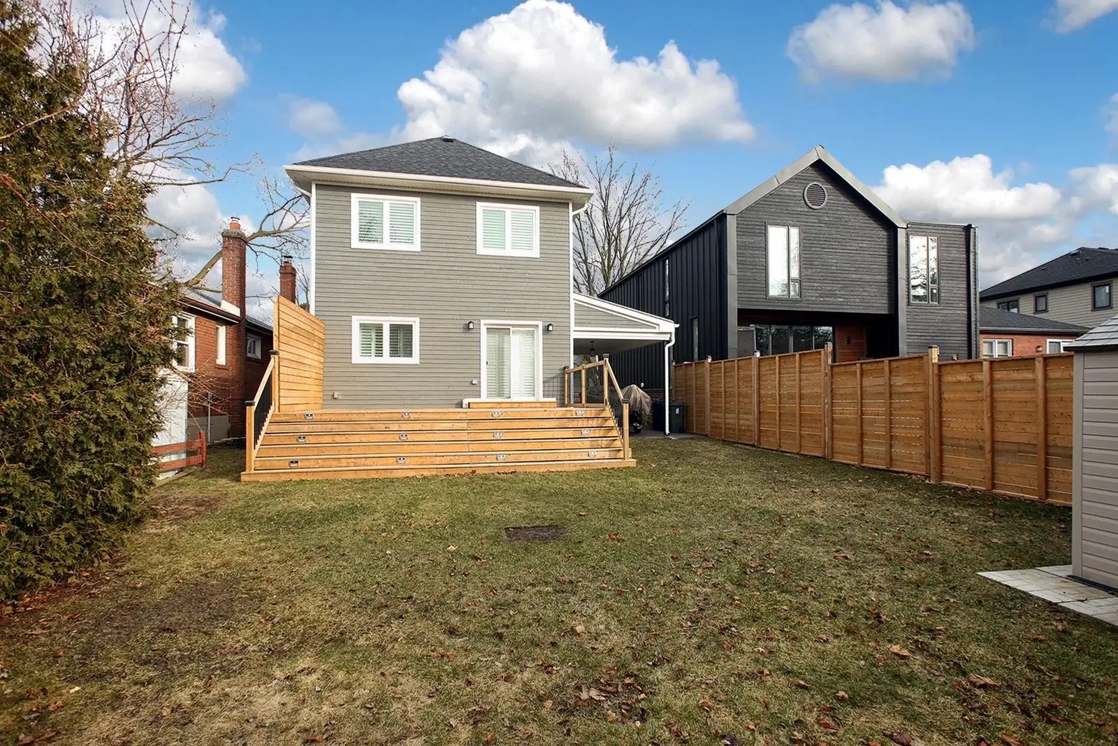 Rear exterior with greige siding, broad wood deck steps, fenced lawn and bright blue sky.