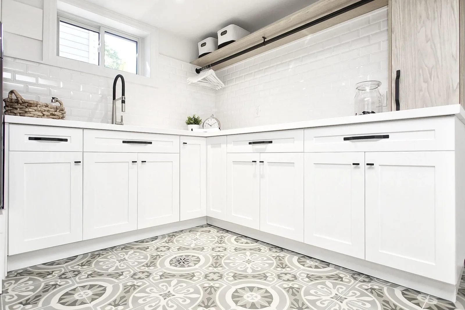 Bright white laundry room with shaker cabinets, black hardware, subway tile, and patterned grey floor tile.