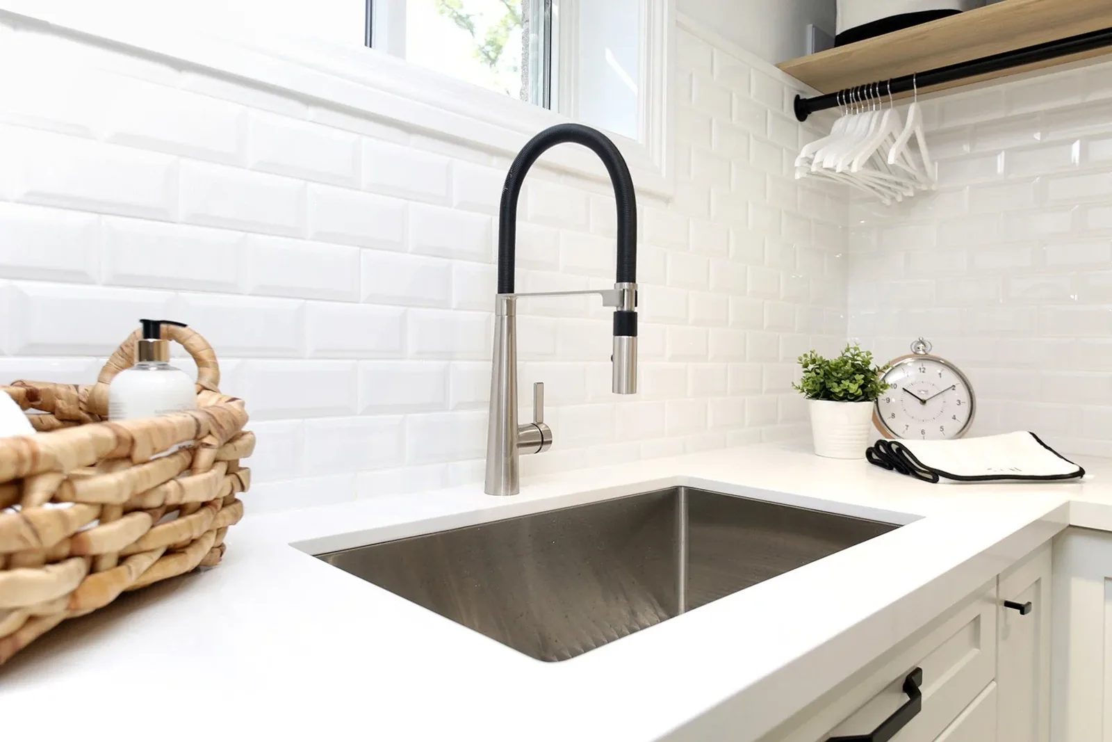 Bright laundry room detail with white tile, quartz counter, black faucet, and hanging rail above the sink.
