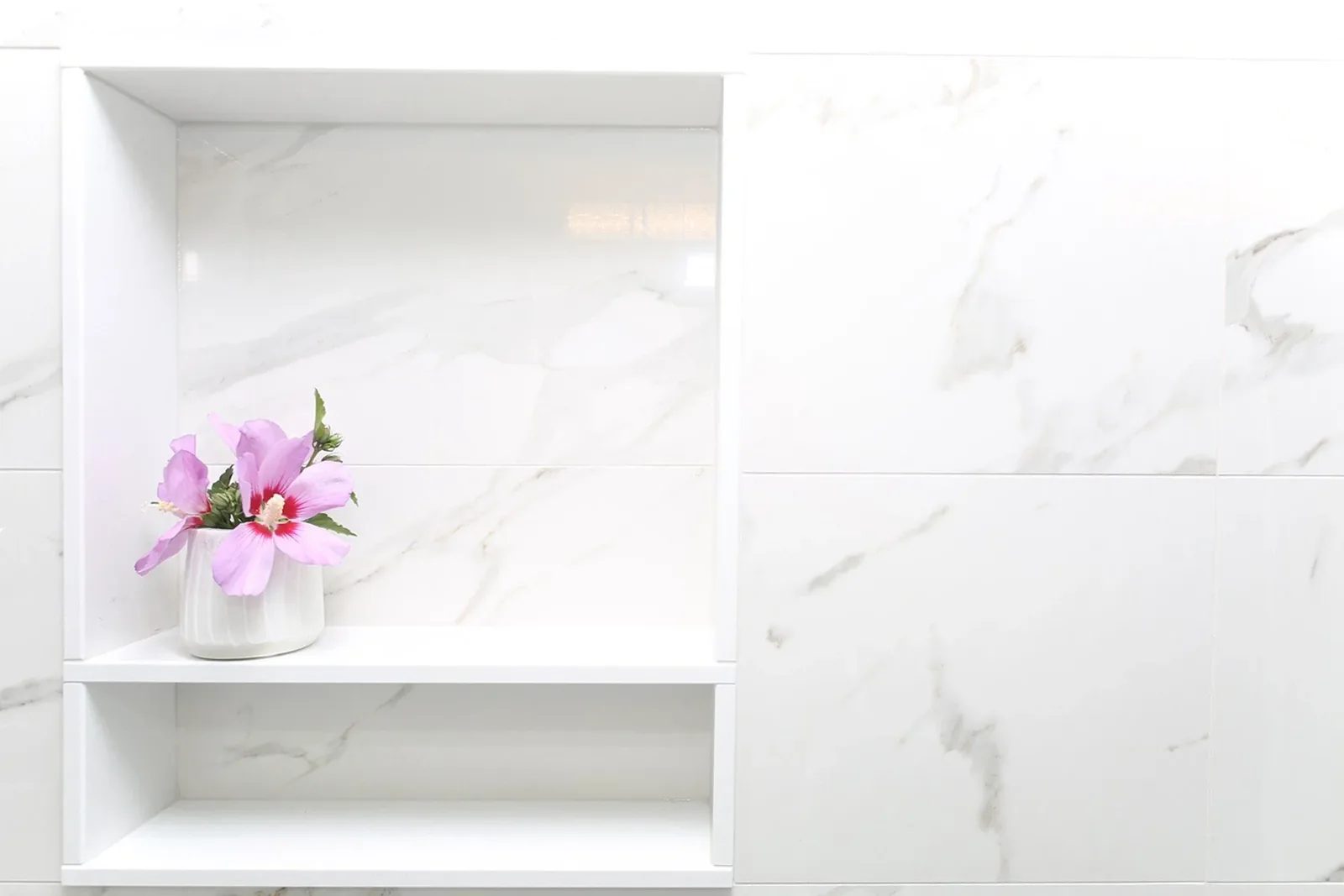 White recessed bathroom niche with marble-look tile and pink flowers, styled as a clean renovation detail.