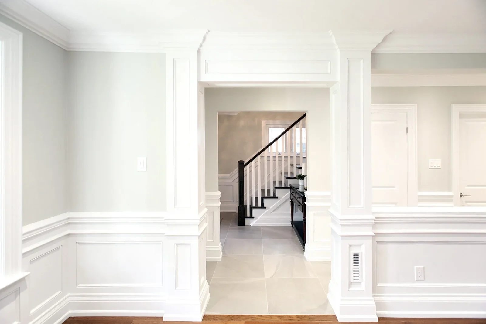 Bright centre hall with white panel moulding, soft grey walls, and a staircase framed by custom millwork.