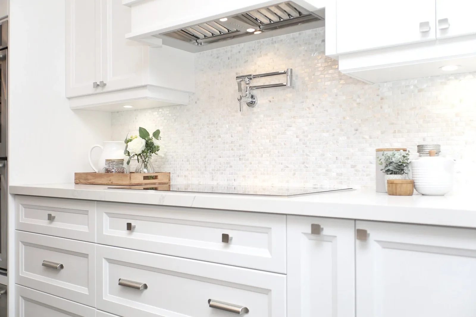 Bright white kitchen detail with quartz counter, mosaic backsplash and a wall-mounted pot filler.