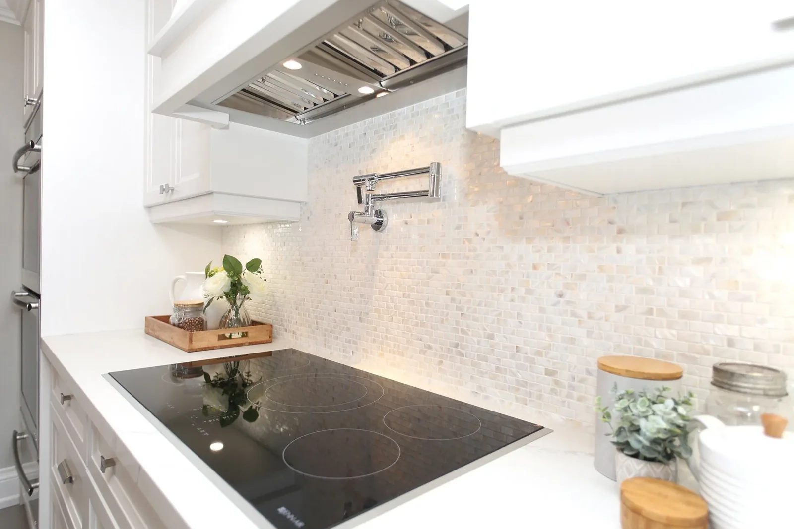 Bright white kitchen detail with quartz counter, mosaic tile backsplash, pot filler and sleek black cooktop.
