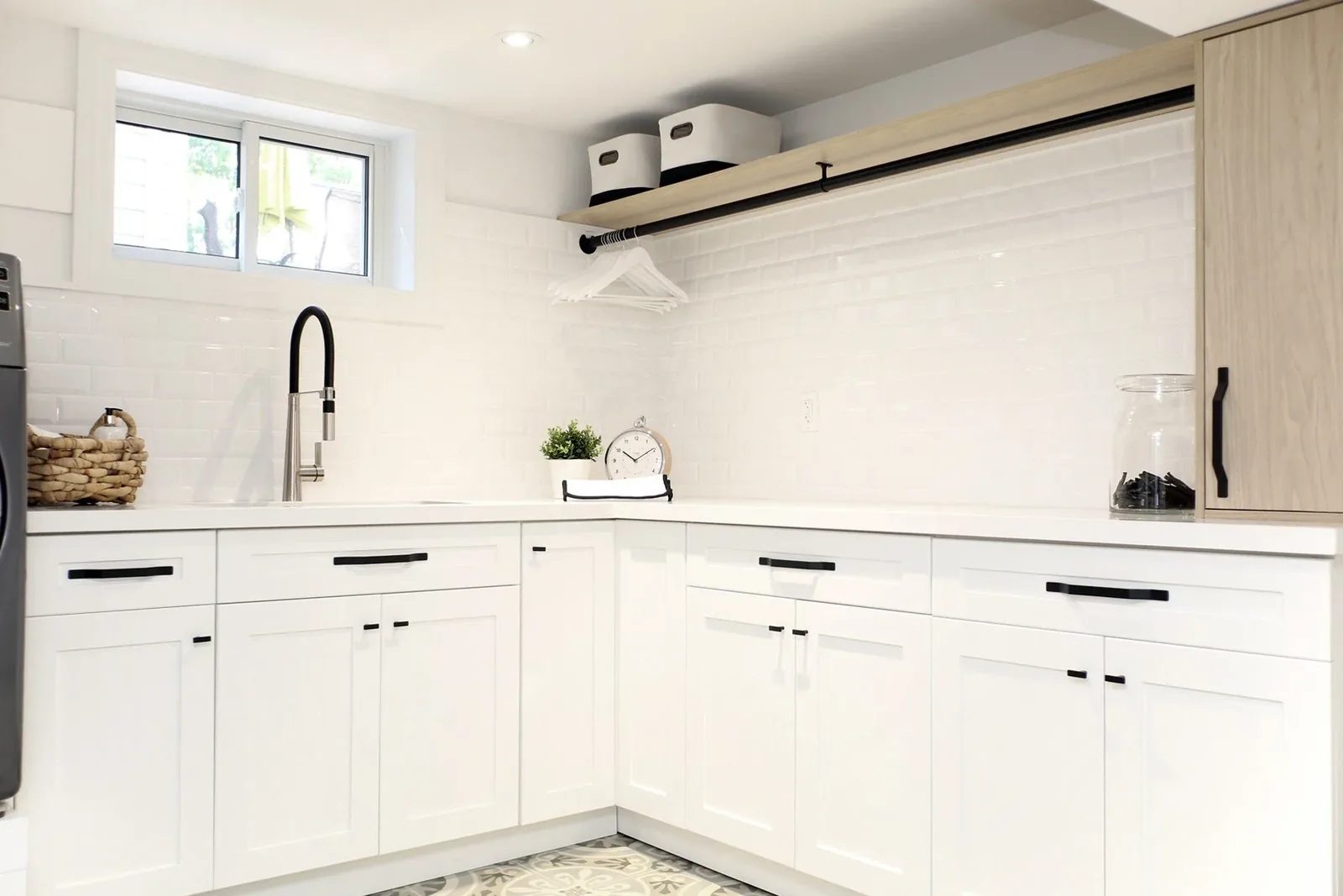 Bright laundry room with white shaker cabinets, black hardware, a wall drying rail and glossy tile.