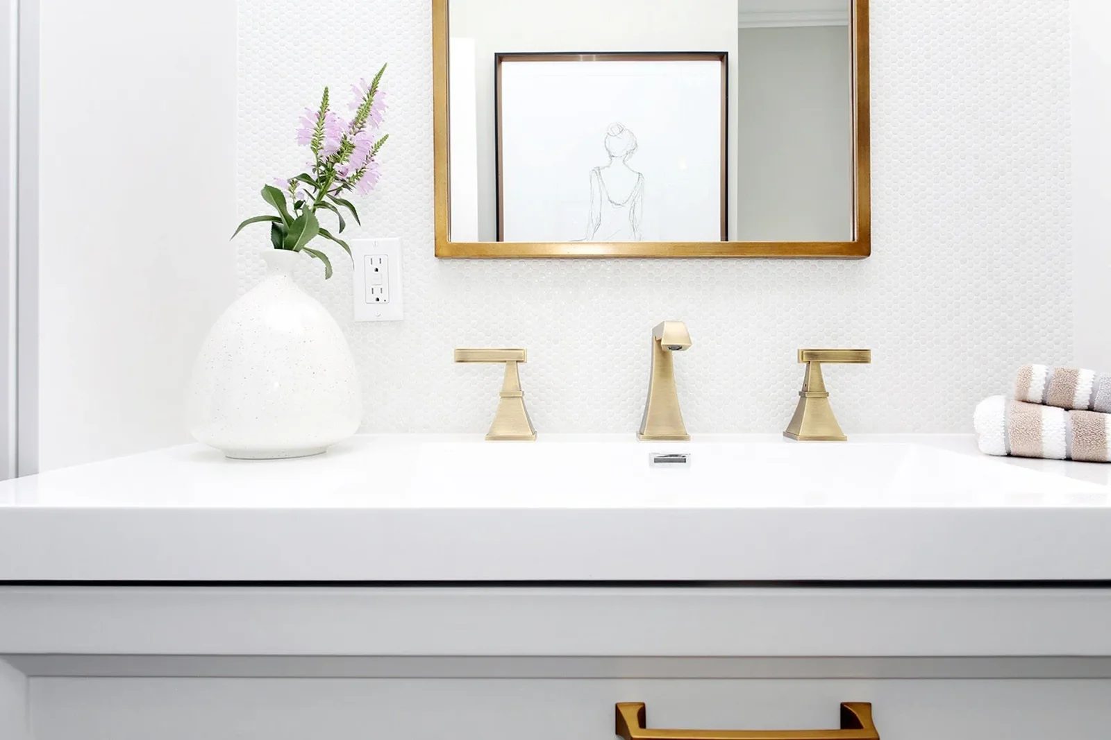 Soft white bathroom vanity with brass fixtures, a framed mirror, and neatly organised folded towels.
