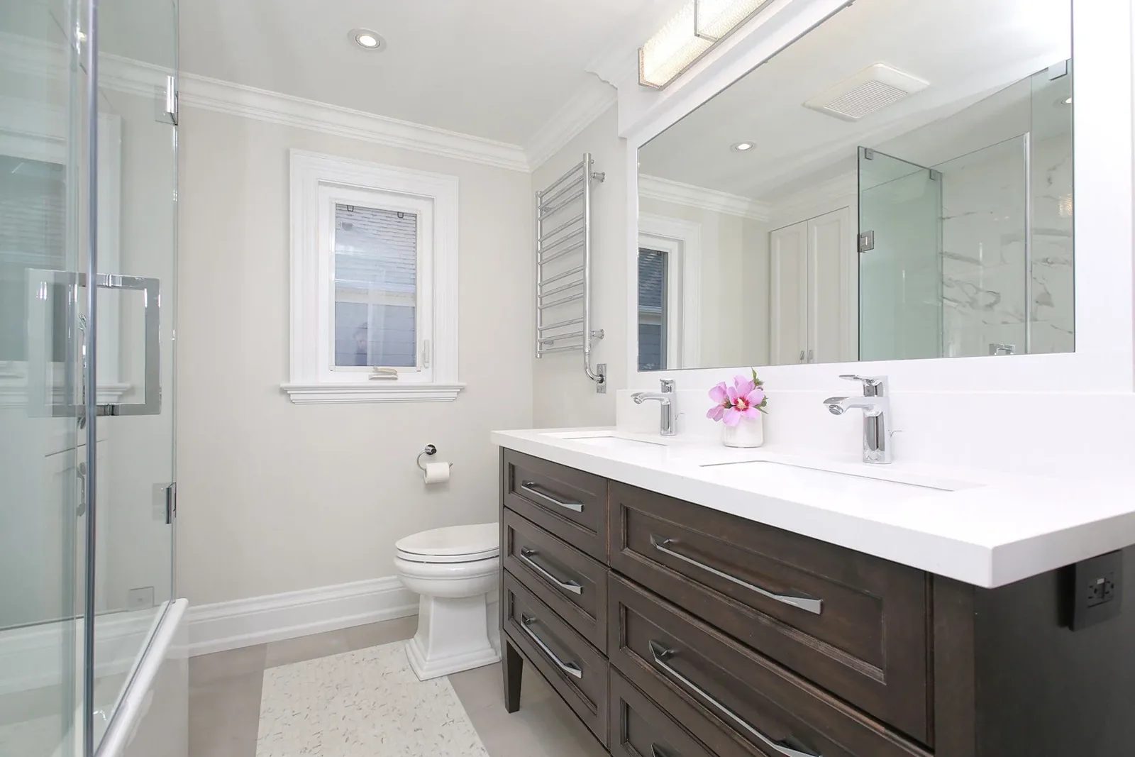 Bright renovated bathroom with a dark wood double vanity, glass shower, white walls and chrome fixtures.