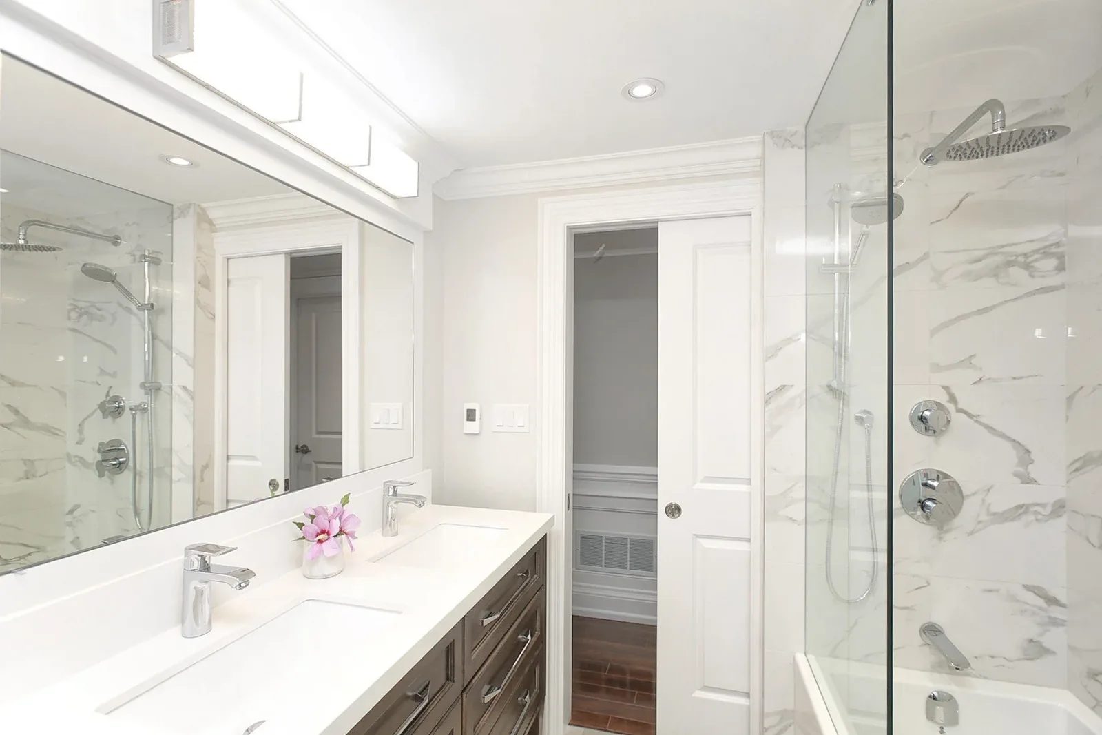 Bright renovated bathroom with a double vanity, marble style shower walls, and chrome fixtures.