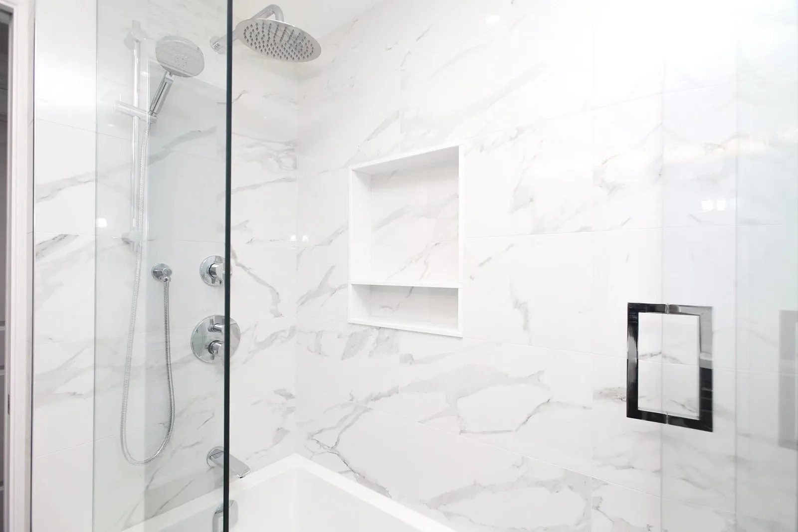 Bright white marble look shower with a glass enclosure, tub base and recessed wall niche.